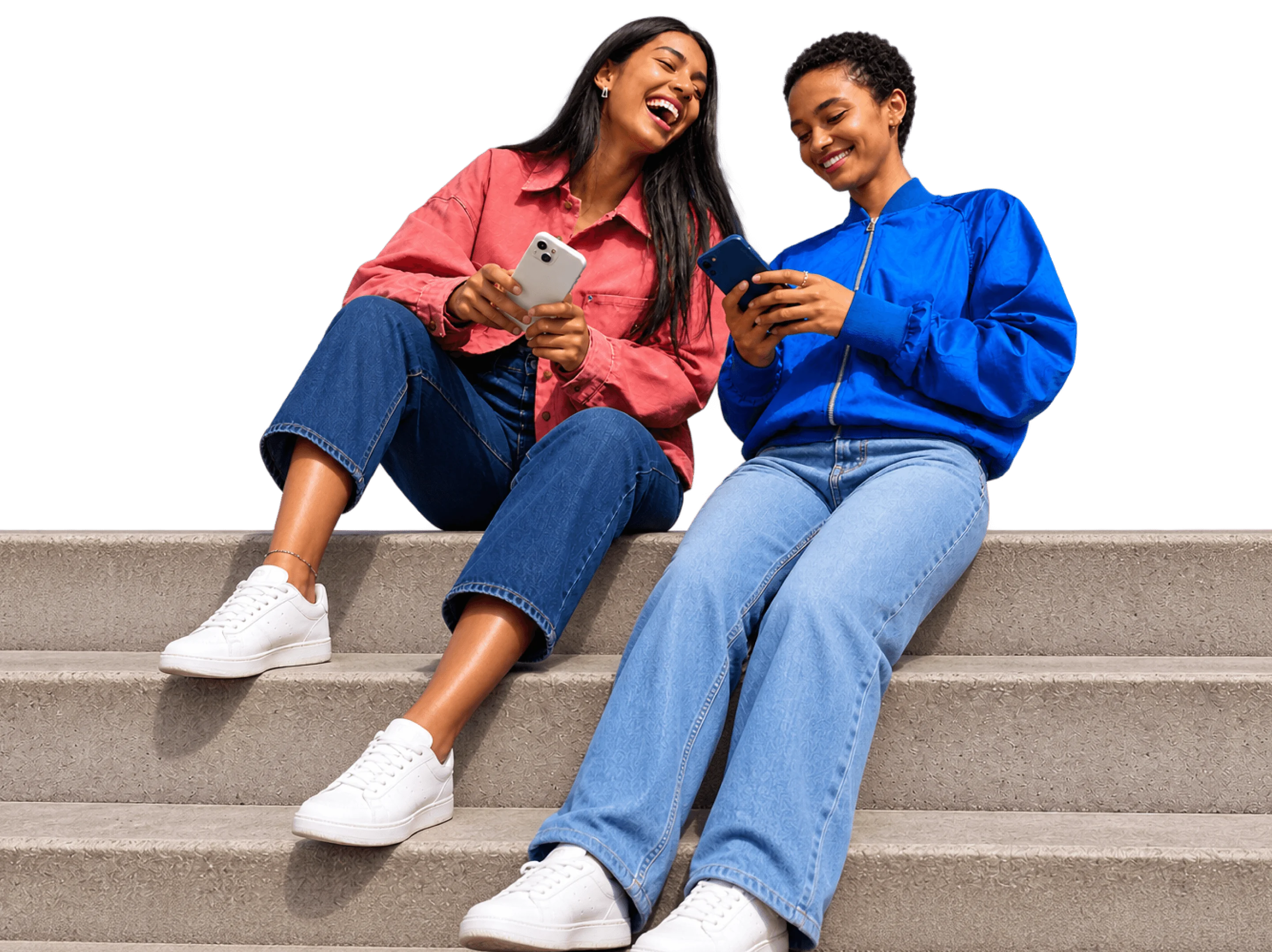 Two friends on a set of steps, laughing at something on their phones.